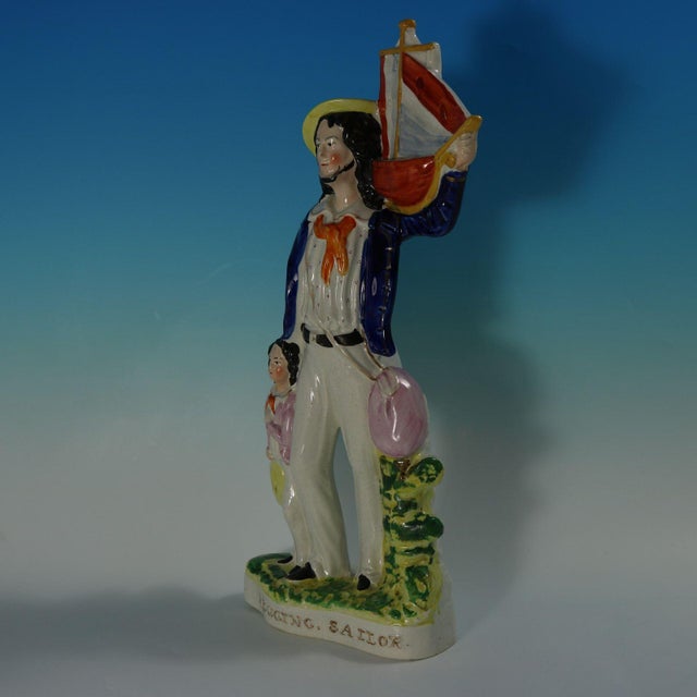 Staffordshire Pottery figure with a maritime theme which features a sailor holding a sailing boat on his shoulder, with a...