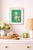 A pink ceramic poodle with vivid green beaded fur is photographed against a saturated green background, creating a playful...