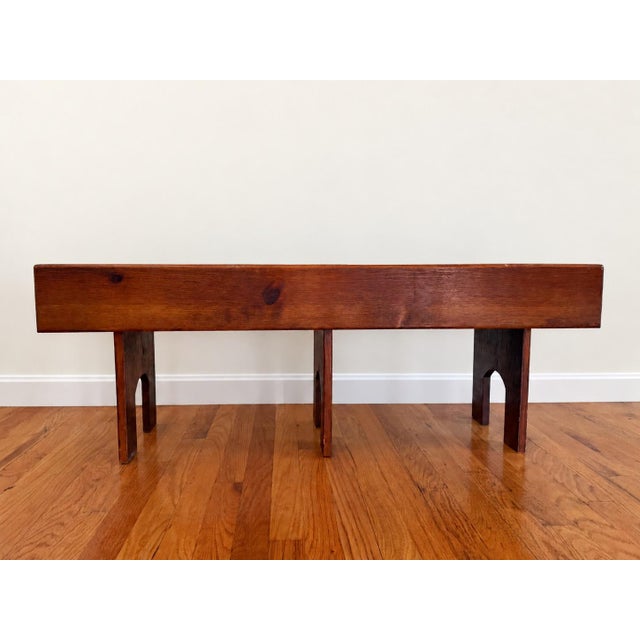 A distinctive mid-century wooden bench with a striking architectural silhouette. Its elongated seat and deep apron rest on...