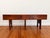 A distinctive mid-century wooden bench with a striking architectural silhouette. Its elongated seat and deep apron rest on...