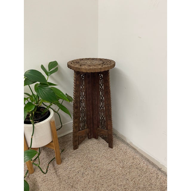 Hand-carved wooden pedestal table featuring intricate pierced carving and a circular top with decorative bone inlay. The...