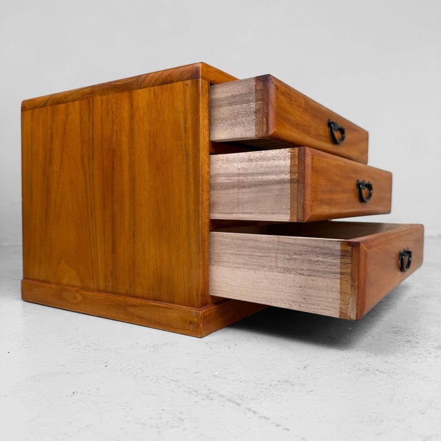 An elegant small Japanese desktop chest with three drawers, warm honey-coloured wood tones and subtle black metal...