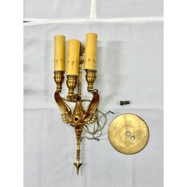 Eye-catching Empire-style three-light wall sconce in gilt brass, featuring a finely detailed spread-winged bird body and...