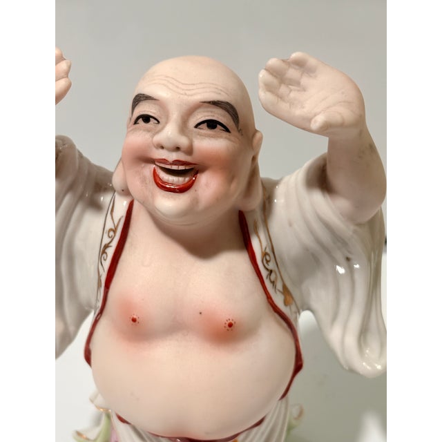 This vintage porcelain Laughing Buddha figurine features a joyful expression, raised arms, exposed belly, and flowing robe...
