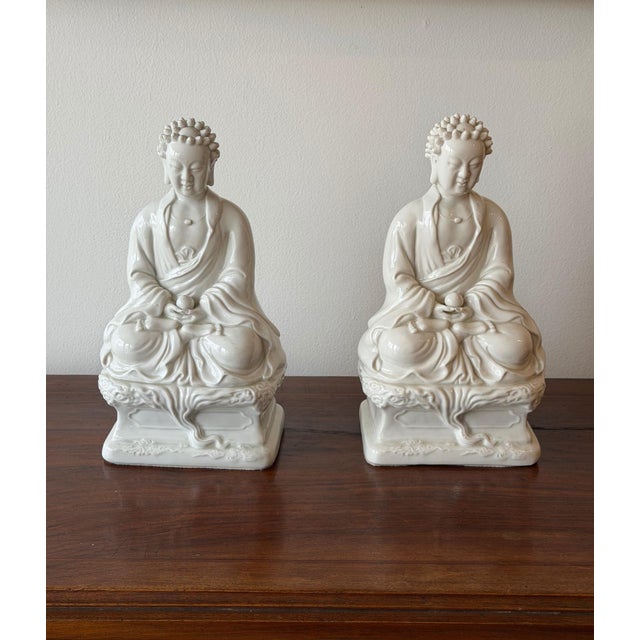 A intricate pair of vintage porcelain Blanc de Chine-style Buddha figures, each rendered in a classic seated meditation...