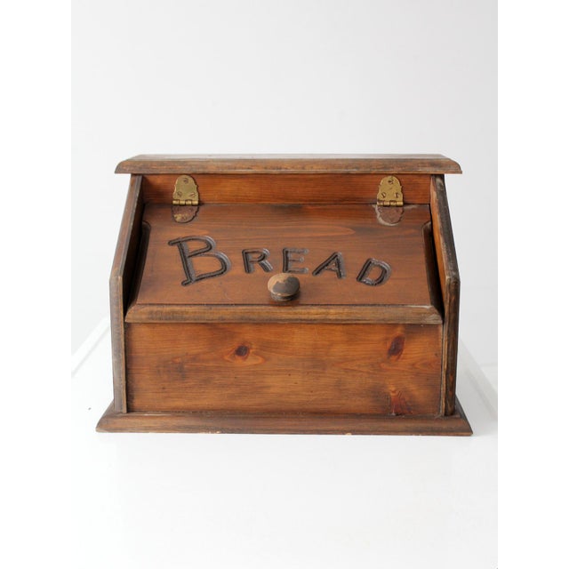 This vintage wood bread box features a hand-carved 'BREAD' inscription and a warm, rustic finish. It's a charming piece...