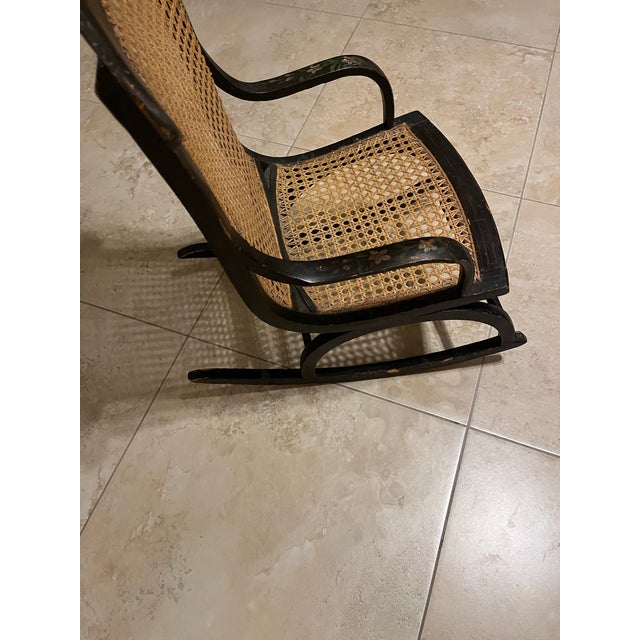 This is an antique American 19th-century child's rocking chair, featuring a caned back and seat. The frame is likely...