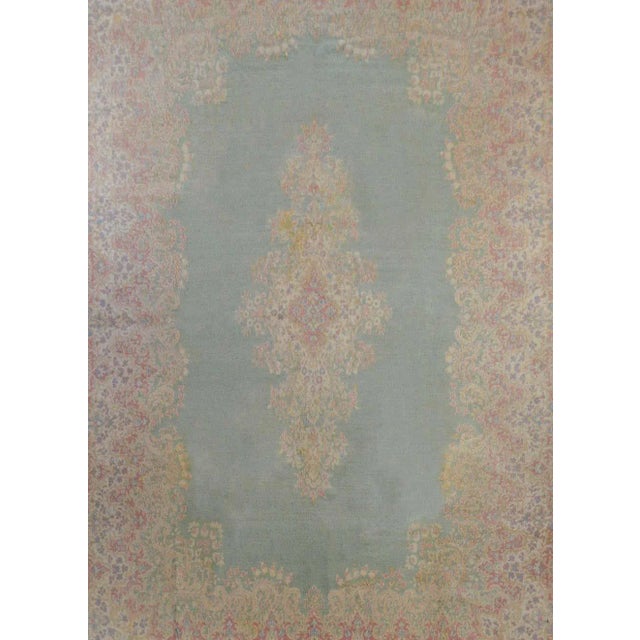 A wonderful early 20th century Persian Kirman rug with a large floral medallion woven in muted indigos, greens, oranges,...