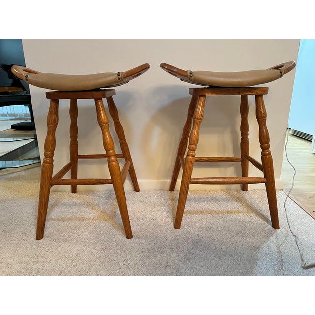 These 2 are Amish handcrafted swivel saddle bar stools featuring a light brown wood base and upholstered leather seats...