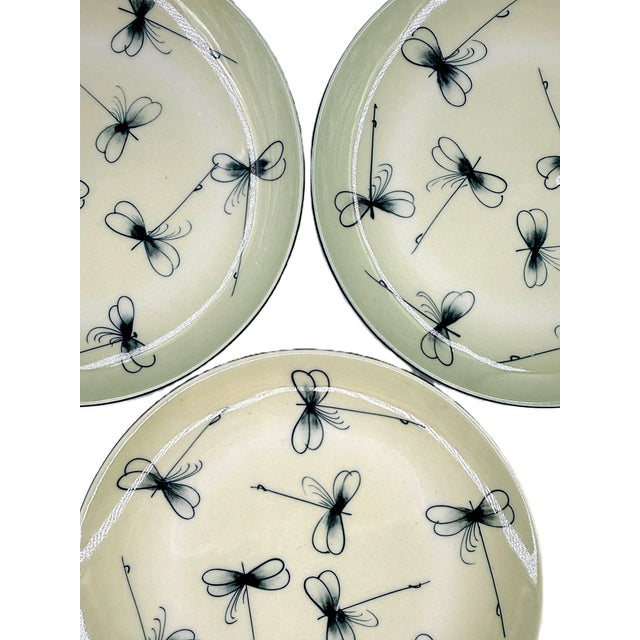 A charming set of four Bat Trang dessert plates featuring delicate hand-painted dragonflies scattered across a warm ivory-...