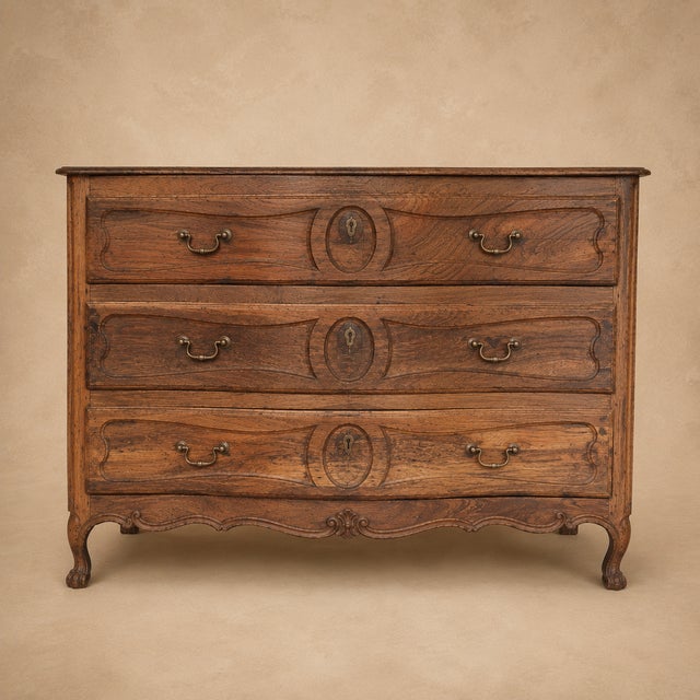 A handsome 19th century French provincial oak commode with a subtly serpentine front, three drawers, shaped apron carving,...