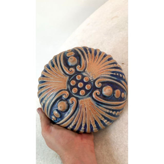Handmade ceramic tripod bowl featuring a textured exterior with raised ribs, blue-green glazing, and a deep reddish-...