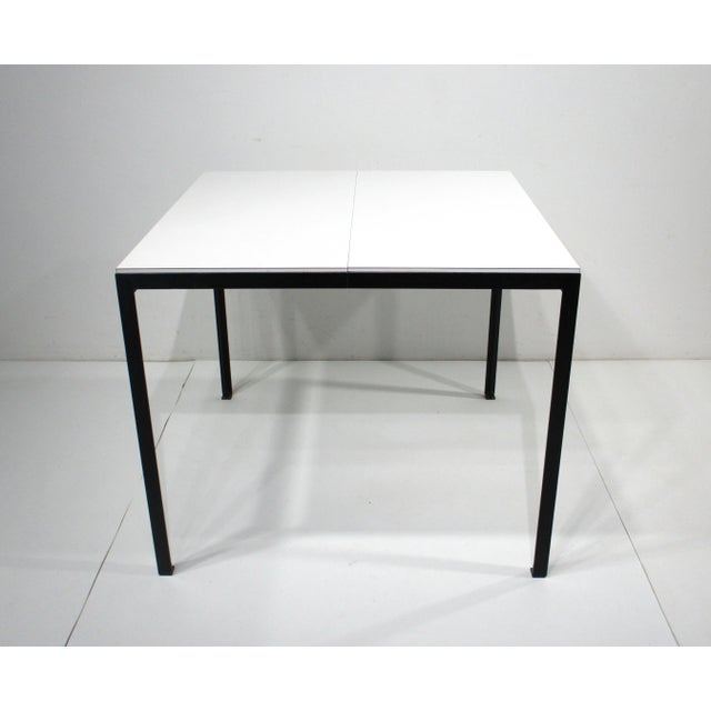 A satin black steel T Angle framed extension dining table with white Laminate top having a pop up folding leaf which...