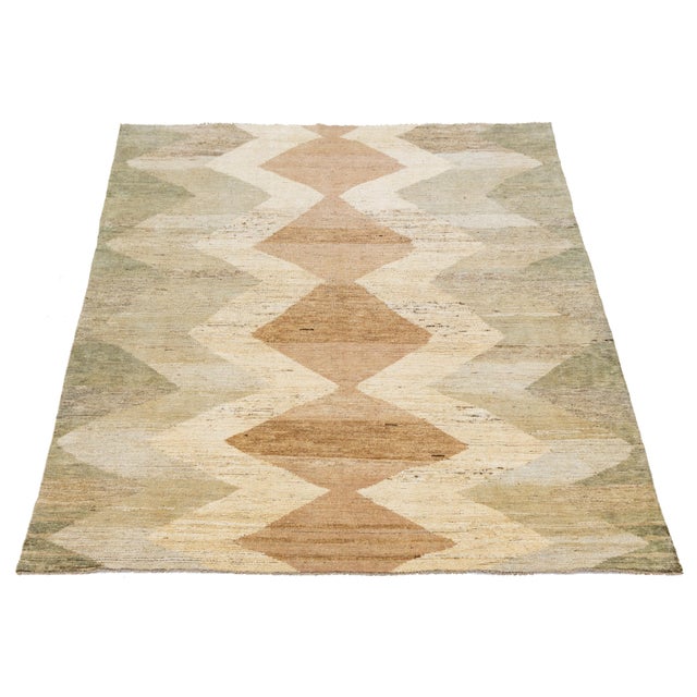 Flatwoven Moroccan-style wool rug showcasing earthy tones of beige, brown, and sage green. The bold central diamond...