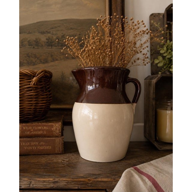 This handsome vintage American pottery pitcher features a classic two-tone glazed finish with a rich chocolate brown upper...
