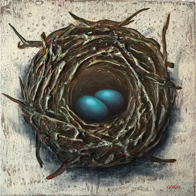 This mixed media piece presents a meticulously crafted bird's nest cradling two vibrant blue eggs at its center. The...