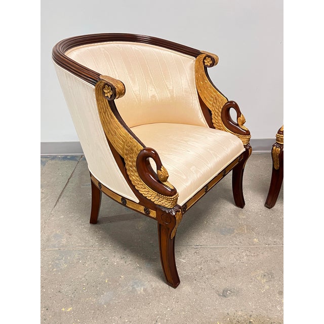 A pair of Maitland-Smith empire bergère chairs in parcel gilt with hand-carved swan-neck armrests and silk grosgrain...