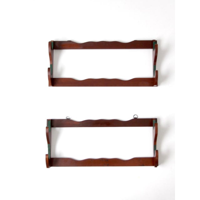 A refined pair of mid-century wooden wall racks featuring warm stained wood, sculpted rests, and softly scalloped rails...