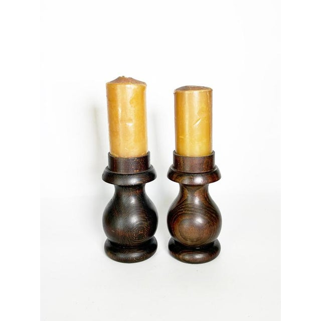 An elegant pair of solid turned-wood candlesticks featuring a beautiful dark brown patina that highlights the wood's...