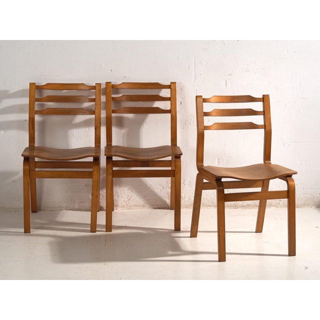 A set of three antique dining chairs in beech and moulded plywood, with a three-rail shaped back and a press-formed saddle...