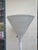 This 1970s torchiere is a sober sculptural floor lamp. A deep white trumpet shade rises from a slender tapered stem on a...
