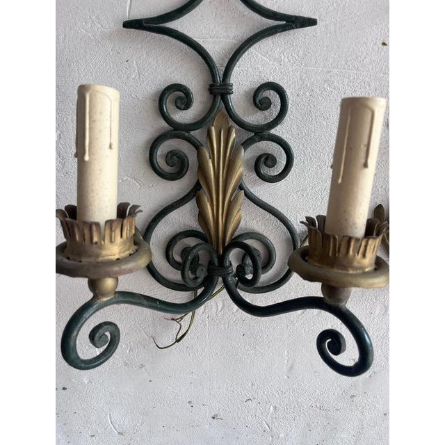 Elegant pair of handcrafted wrought iron wall sconces featuring graceful scrollwork and decorative gilt acanthus leaf...