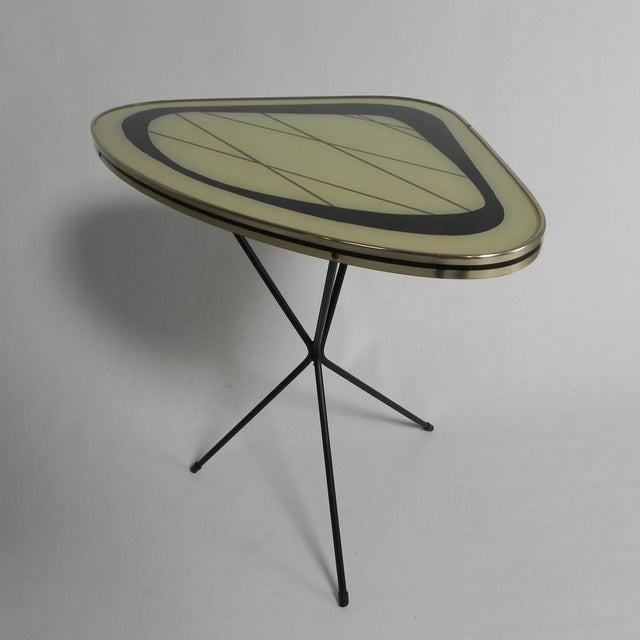 This table is also known as the "Expo 58" table. The tabletop features typical 1950s decoration and rests on crossed black...