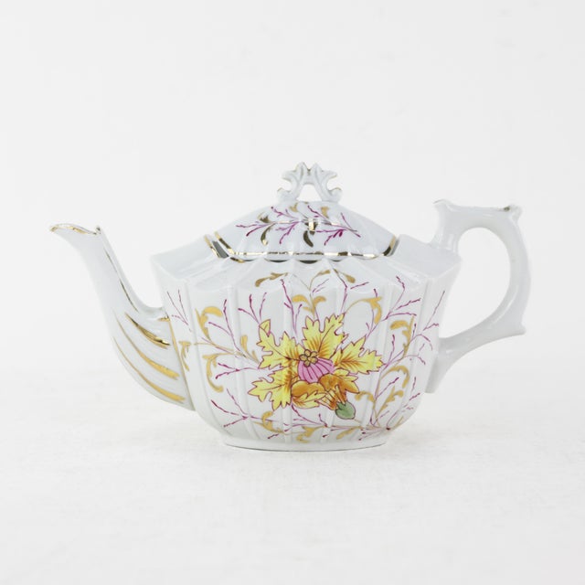 This exquisite antique porcelain tea set includes a teapot and sugar bowl, both featuring a delicate floral design, gold...