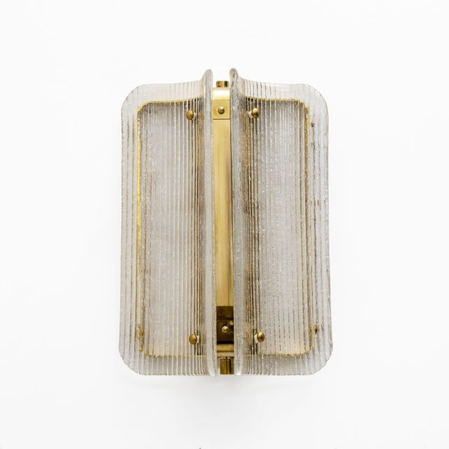 An elegant pair of italian wall sconces made of curved and fluted murano glass panels in a refined shade of clear. The...
