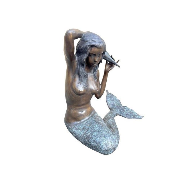 A striking life-size bronze mermaid sculpture, beautifully modelled in a seated pose while holding a large conch shell...