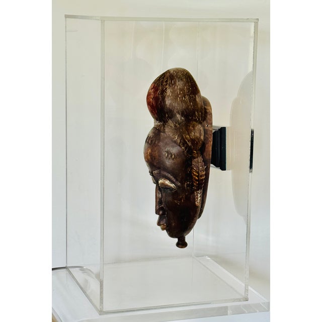 A Baule people carved wood portrait mask. Ivory Coast from the mid 20th century. Encased in a lucite museum quality...
