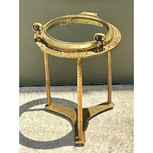 This vintage brass and glass porthole accent table brings authentic mid-century maritime design to any interior, its round...