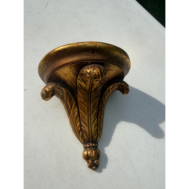 Vintage Italian Florentine-style wall bracket shelf with a distressed gilt finish and classic acanthus leaf detailing. A...