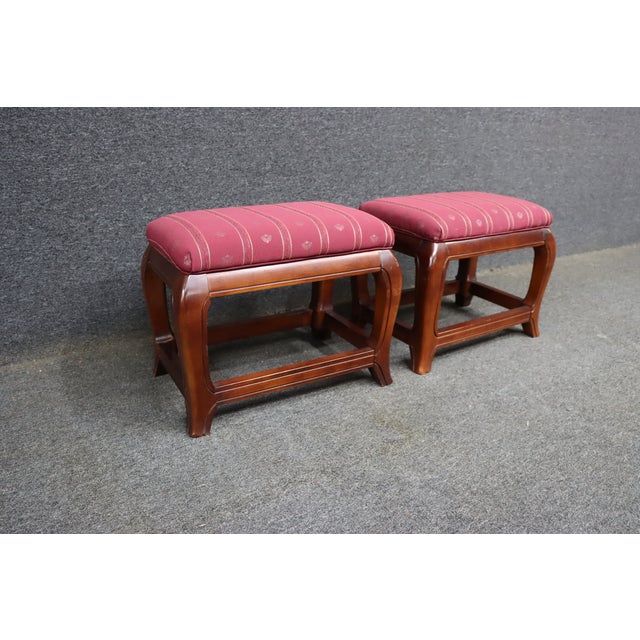 Pair of Ethan Allen upholstered footstools featuring a rich cherry-toned wood frame and burgundy patterned upholstery with...