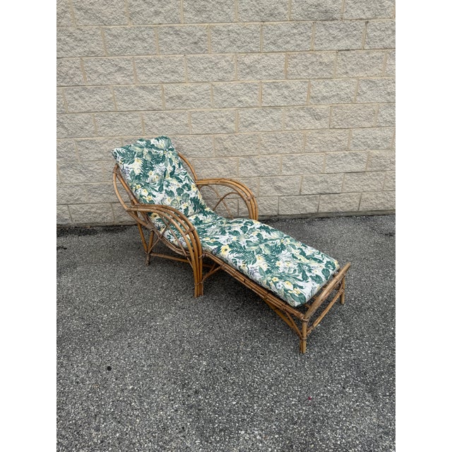 Vintage rattan chaise lounge with curved arms and woven cane details. The frame features an extended footrest and...