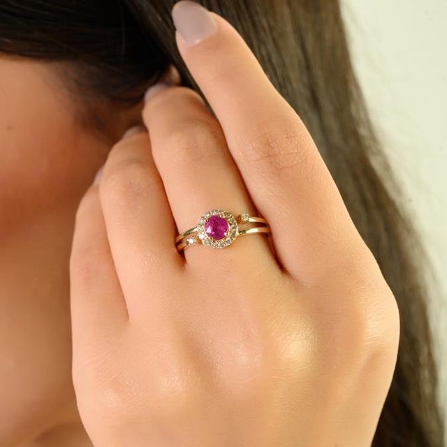 This vintage-inspired halo ring features a round-cut ruby totaling approximately 0.60 carats, elegantly set in 14K yellow...