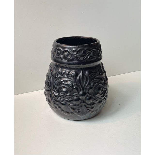 Unusual relief earthenware vase with floral patterns. Black paint over maroon paint. Designed and manufactured by...