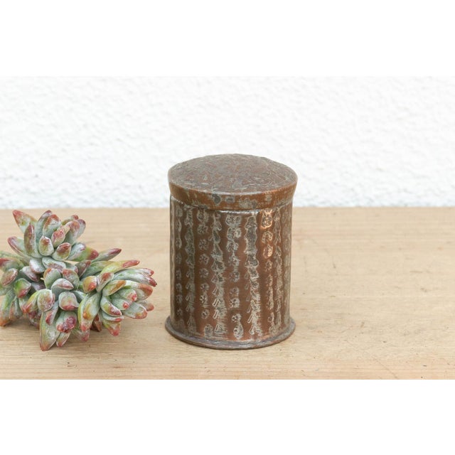 This petite cylindrical box is defined by its textured surface, featuring vertical columns of hand-hammered stylized...