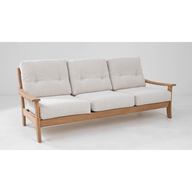 An oak three-seater sofa made in mid-20th century France. Dynamic shapes and a homey natural color palette make an...