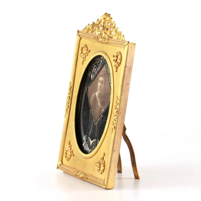 Photo frame of gilded bronze in the style of neoclassicism. Decorated with wreaths, flower garlands and ribbons.