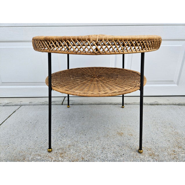 A great looking round woven rattan or wicker two-tiered side table with black metal supports and brass ball feet. This...
