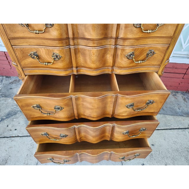 Elegant John Widdicomb tallboy dresser is crafted from wood with a warm honey finish. This French Provincial style chest...