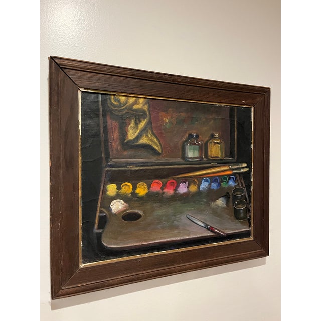 Charming mid century still life featuring a traditional artist's palette lined with vibrant pigments, brushes, and studio...