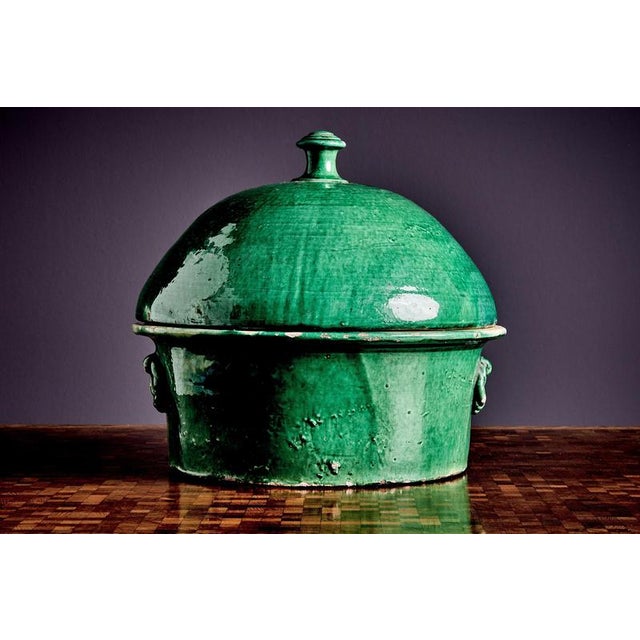A hand-made earthenware pot with a domed lid, ring handles, and a rich green glaze. Visible wear, craquelure, and firing...