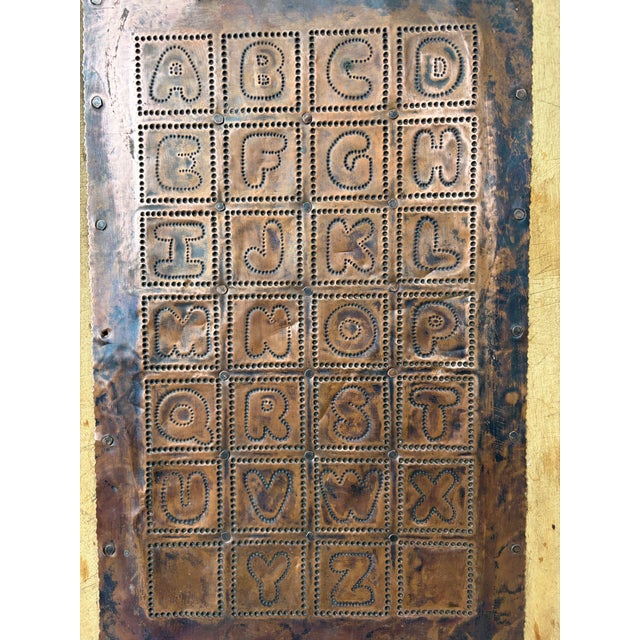 Antique, primitive, hand made wooden cutting board with a copper hand punched sheet of the alphabet attached in the...