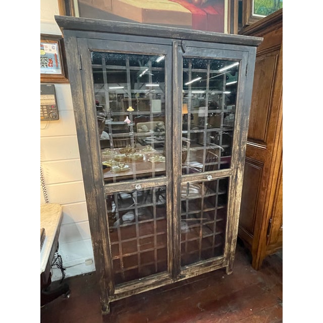 Rustic two-door bookcase cabinet with glazed panel doors, geometric wood muntins, and a molded cornice with a naturally...