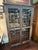 Rustic two-door bookcase cabinet with glazed panel doors, geometric wood muntins, and a molded cornice with a naturally...