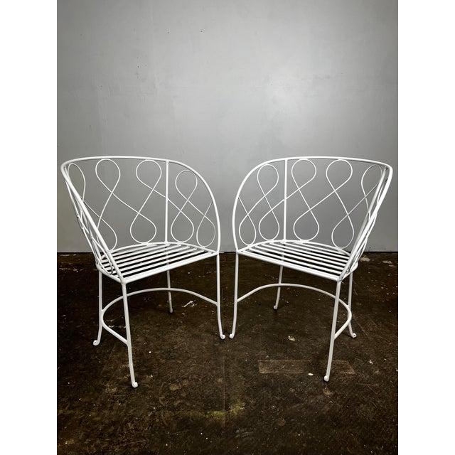 Vintage pair of mid century wrought iron curlicue loop chairs. Two pairs available. Curved backs with loop design. Refined...