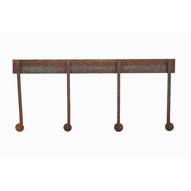 Industrial style wall hook rail with four peg hooks. It is made of wrought iron with a distressed rusted finish. It has a...