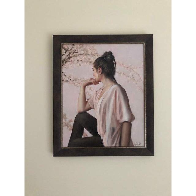 The painting depicts a young woman lost in contemplation, her profile framed against a soft, pastel background adorned...